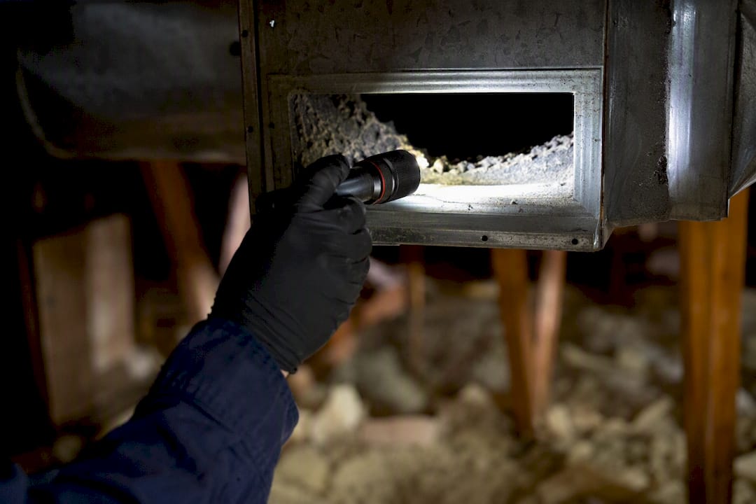 Technician inspecting furnace duct with flashlight